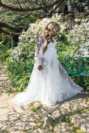 Woman in a white dress standing in a garden with white flowers and a green bench. Vote Ruby Lynn – Baby of the Year 2025 campaign