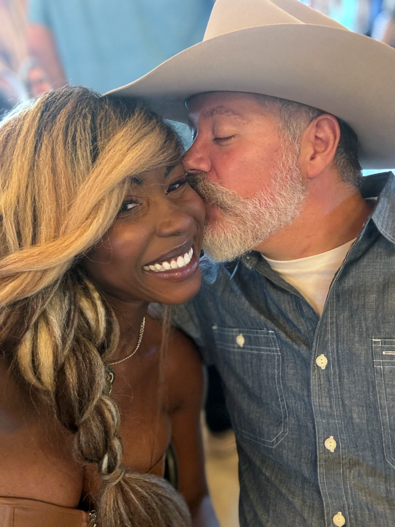 Man and woman embracing, both wearing cowboy hats and casual clothing. Vote Ruby Lynn – Baby of the Year 2025 campaign